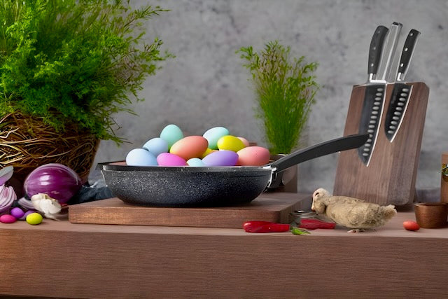 CAROTE® Granite - kleine Pfanne aus geschmiedetem Aluminium mit bunten Eiern, auf einem Holztisch mit Küchenutensilien und Kräutern.