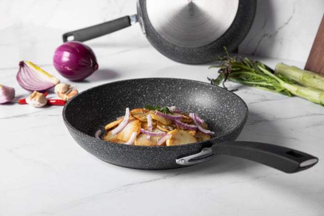CAROTE® Granite - kleine Pfanne aus geschmiedetem Aluminium mit Antihaftbeschichtung und Glasdeckel auf einer Arbeitsplatte.