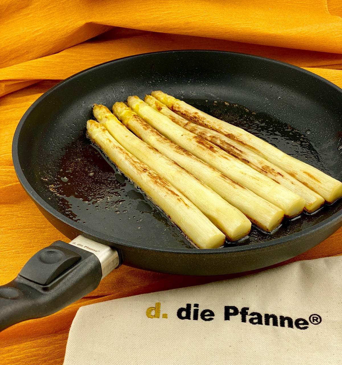 Flache Aluguss-Pfanne der Edition 13 mit abnehmbarem Stiel, gebratener Spargel, orange Hintergrund.