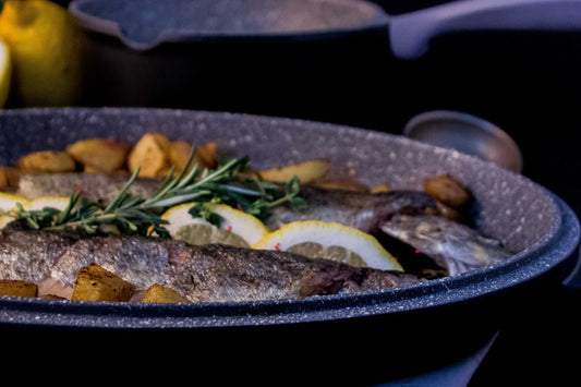 Ovaler Multi-Bräter aus Aluguss mit Fisch, Kartoffeln und Zitronenscheiben, dreilagige Antihaftbeschichtung, vielseitig einsetzbar als Grill- und Fischpfanne.