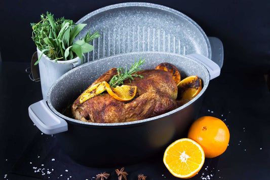 Ovaler Multi-Bräter aus Aluguss mit Braten und Orangen auf dunklem Hintergrund.