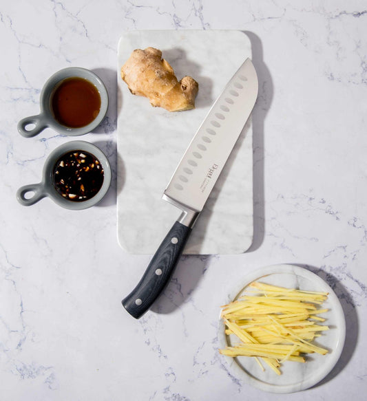 Santokumesser mit Kullenschliff der Serie Elegant von Carote auf Marmorplatte, umgeben von Ingwer und Gewürzen, elegantes Design.