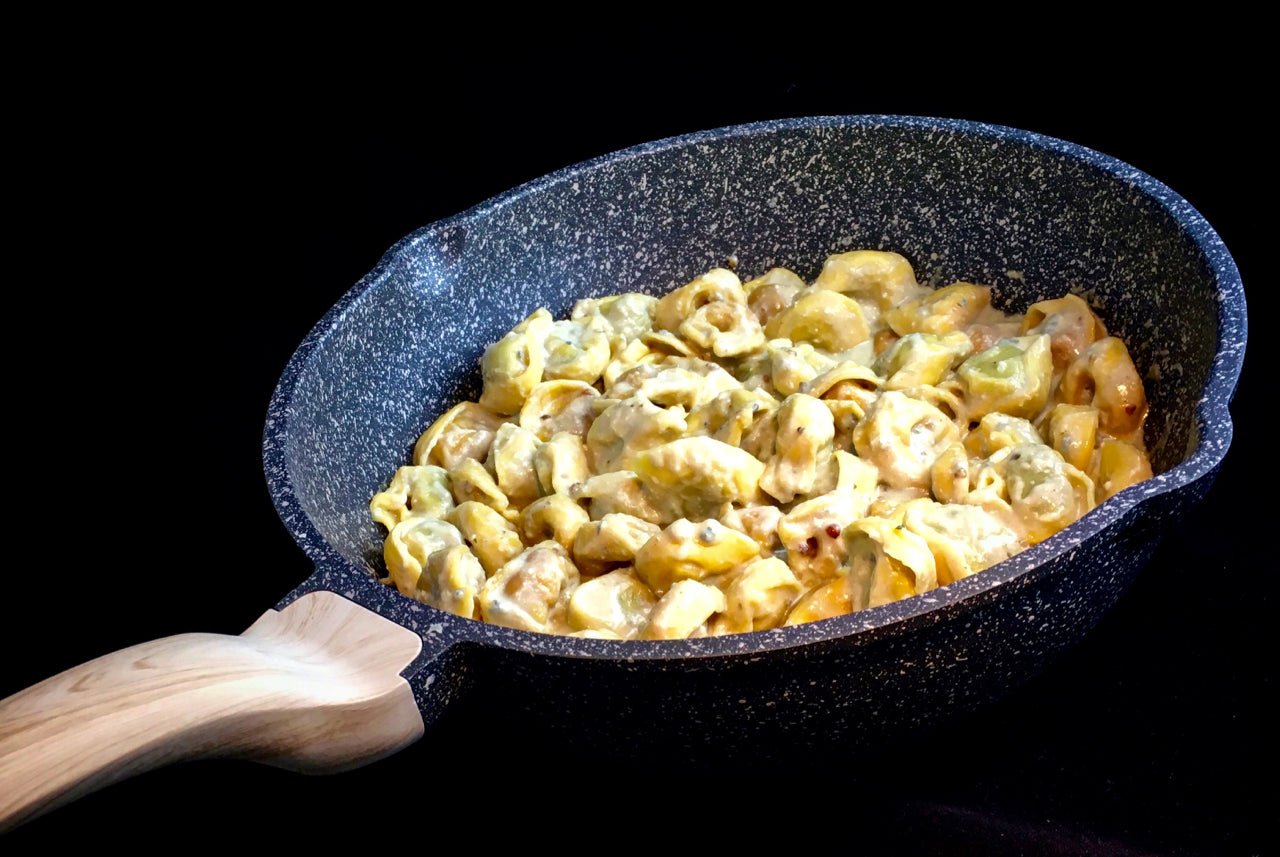 Hochrandpfanne aus Aluguss mit Antihaftbeschichtung und Soft-Touch-Holzeffekt-Stiel von Woody, gefüllt mit cremigem Tortellini-Gericht.