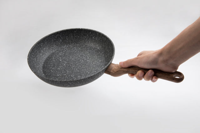 Kleine Pfanne der Serie Air (Durchmesser 20 cm) in rechter Hand vor weißem Hintergrund. Man sieht deutlich das Loch am Ende des ergoomischen Stiels zum Aufhängen der Pfanne.