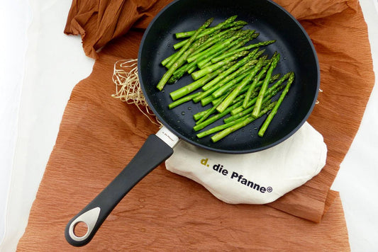 Tiefe Aluguss-Pfanne Edition 13 mit grünem Spargel, abnehmbarem Stiel und antihaftbeschichteter Oberfläche auf rustikalem Untergrund.