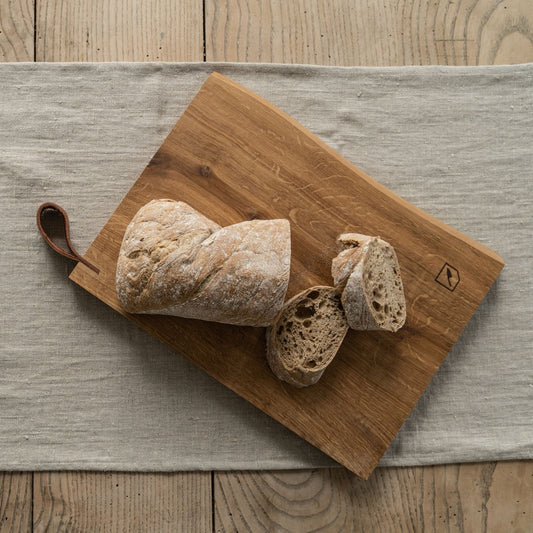Schneidebrett Holz aus massiver Eiche mit Lederaufhänger und rustikalem Design, 40x27x3cm, mit Brot darauf