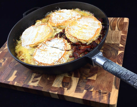 Gusseiserne Bratpfanne mit abnehmbarem Holzgriff, gefüllt mit gebratenem Essen auf hölzerner Unterlage.