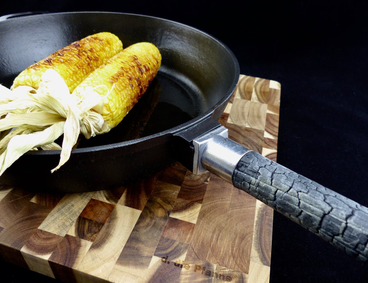 Bratpfanne PUREiron aus Gusseisen mit FlameWood-Stiel und gegrilltem Mais, auf Holzbrett.