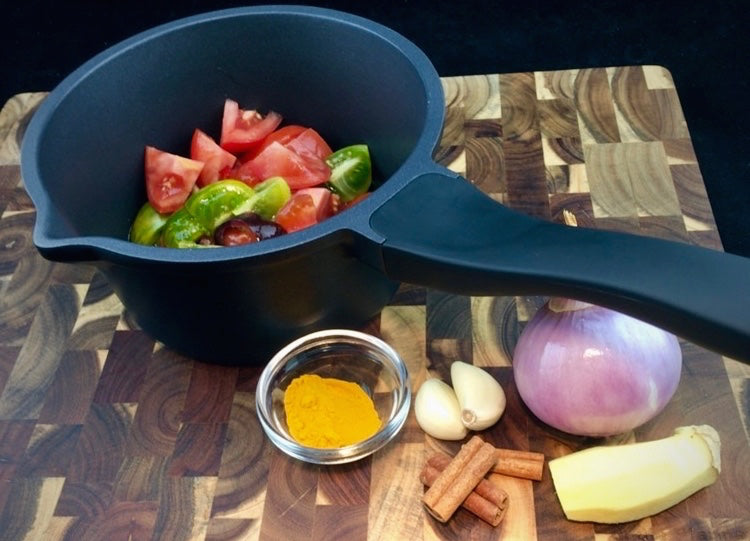 Saucenpfännchen Edition 9 auf Küchenbrett mit Saucenzutaten (Gewürze und Gemüse). Das Pfännchen ist mattschwarz und hat einen schwarzen silikonbeschichteten Bakelitgriff.