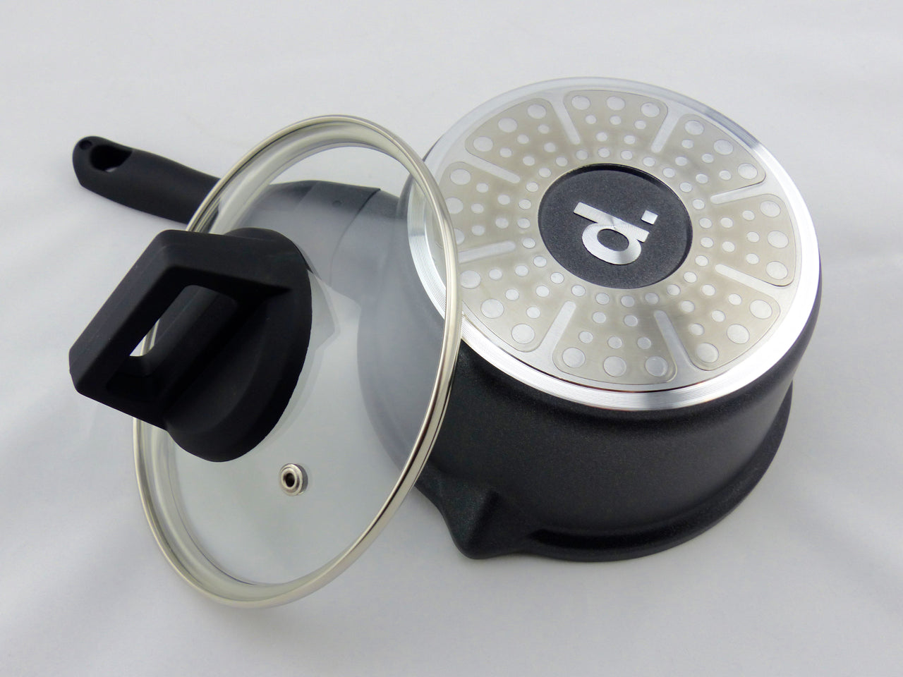 schwarzer Stieltopf Edition 9 im Durchmesser 16 cm in freigestellter Aufnahme von unten. Man sieht den Induktionsboden mit dem Logo 'd.'. Angelehnt ist der dazugehörige Glasdeckel mit Metallrand und Dampfaustrittdüse.