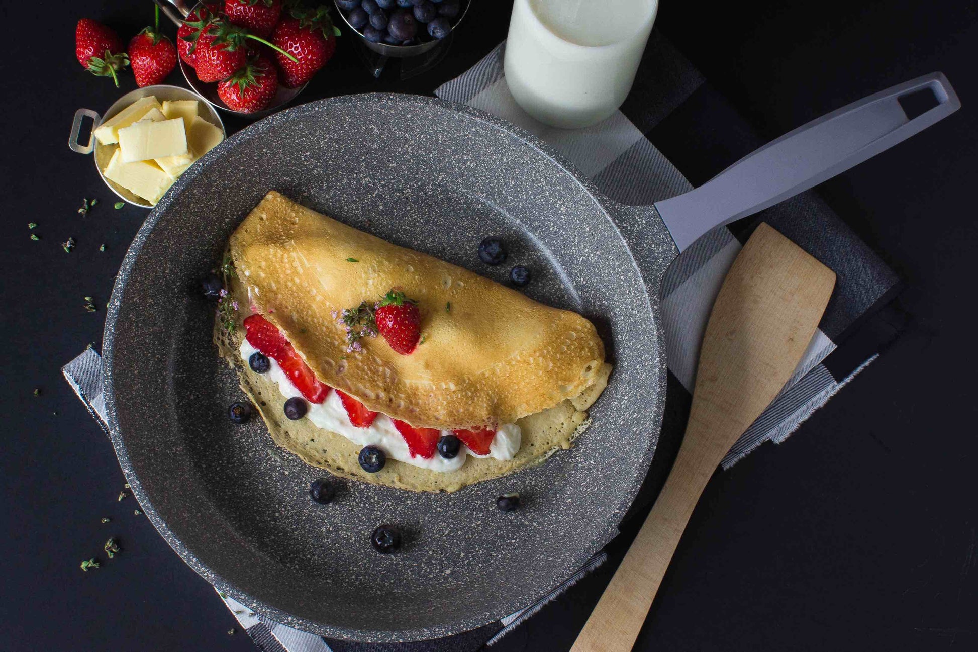 Universalpfanne aus Aluguss Edition 1 mit Crepe, Erdbeeren, Blaubeeren und Sahne. Die Pfanne it innen grau, schwarz und weiß gesprenkelt und hat einen filigranen grauen Stiel aus silikonbeschichtetem Bakelit.